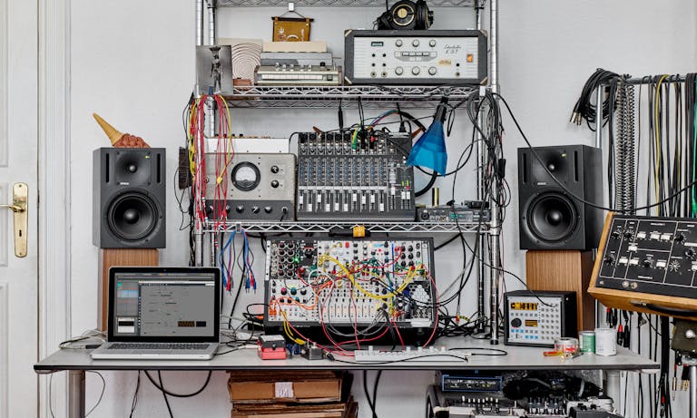 A creative space with a modular synth setup and Ableton Live running Max for Live on the screen.